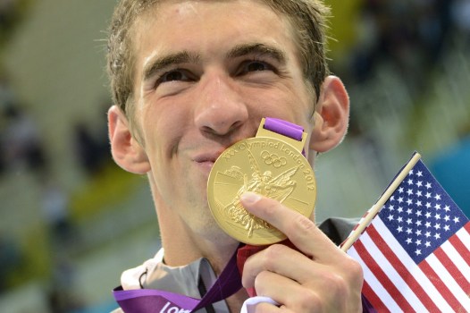 Swimmer Michael Phelps holds an American flag as he kisses a gold medal