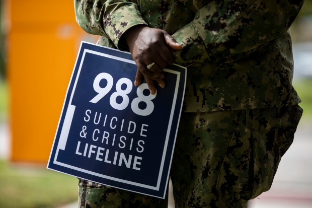 A sailor holds a sign advertising the hotline number for the suicide and crisis lifeline during a press conference regarding mental health in the U.S. Navy at U.S. Fleet Forces Command in Norfolk on Monday, September 25, 2023. (Kendall Warner/The Virginian-Pilot)