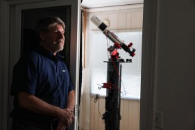 A man stands in front of a window with a telescope